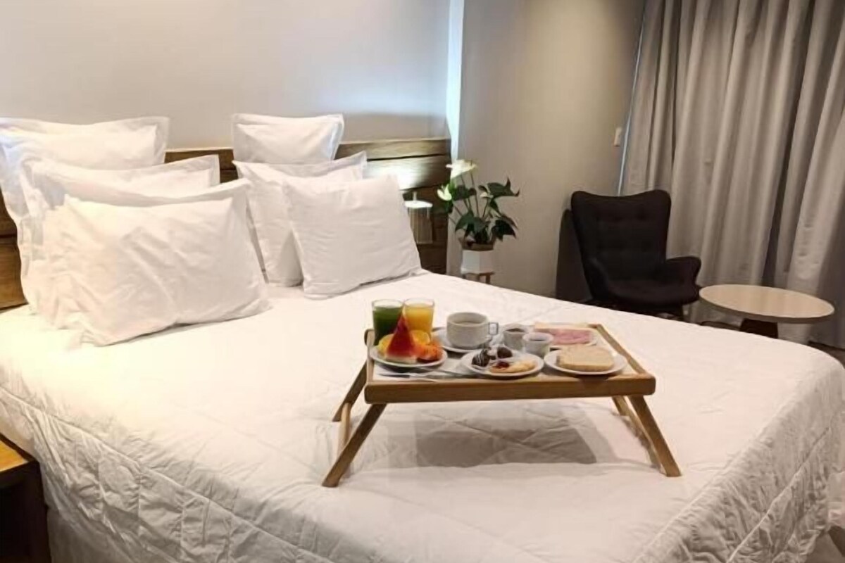 Habitación de hotel con una cama grande, una mesita de noche con una bandeja de desayuno, una silla y una pequeña mesa.
