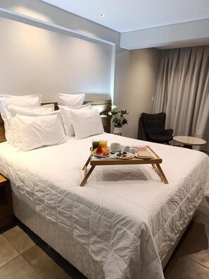 Habitación de hotel con una cama grande, una mesita de noche con una bandeja de desayuno, una silla y una pequeña mesa.