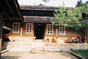 A traditional building with a tiled roof, a stone entrance, and a person seated at a table outside.