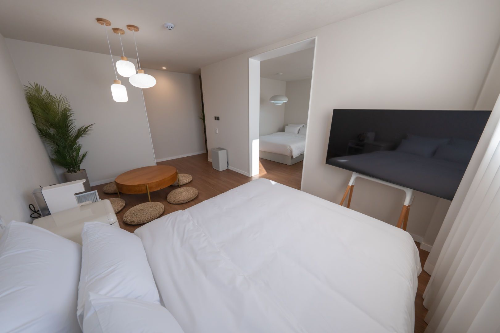 Quarto moderno com uma cama grande, televisão, mesa de madeira redonda e planta em vaso.