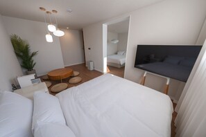 A modern bedroom with a large bed, a TV, a round wooden table, and a potted plant.