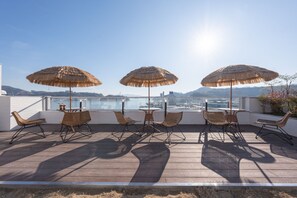 Un espacio al aire libre con sillas de mimbre y sombrillas de paja, con vistas a un paisaje urbano y al agua.