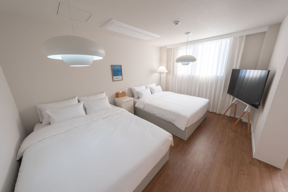 A hotel room with two beds, a TV, and a large window with curtains.