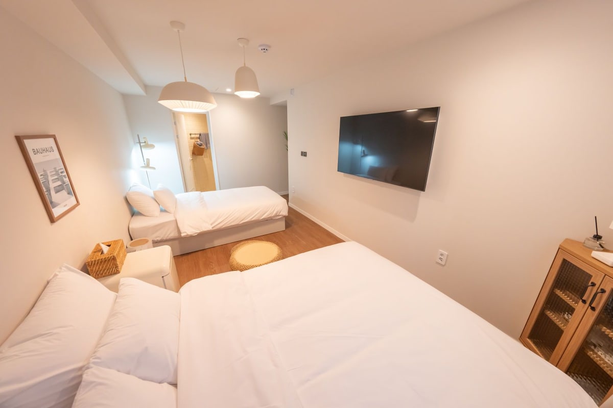 A hotel room with two beds, a flat-screen TV, a wooden cabinet, and a framed picture on the wall.