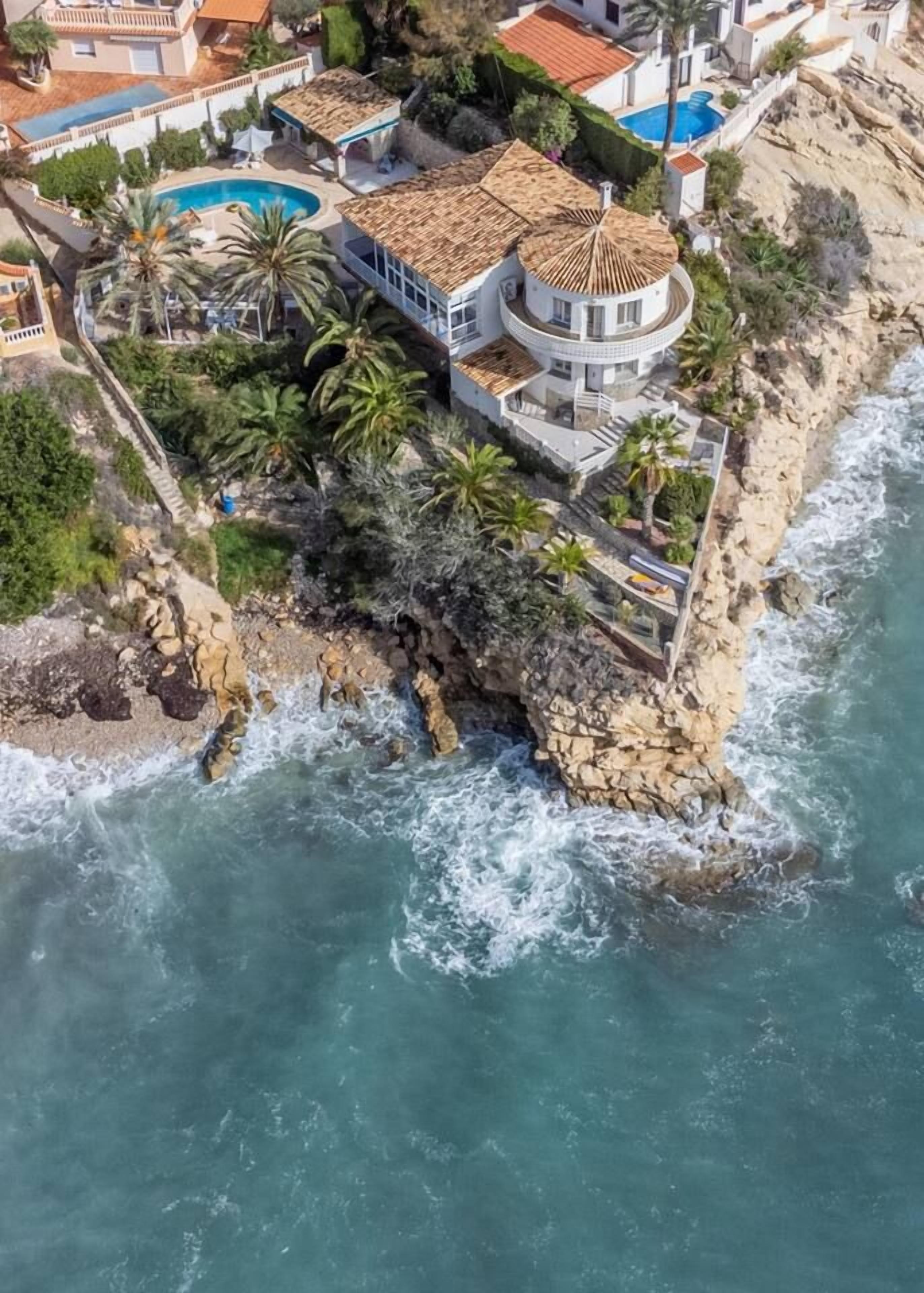A coastal property with a circular building, a swimming pool, and a rocky shoreline.