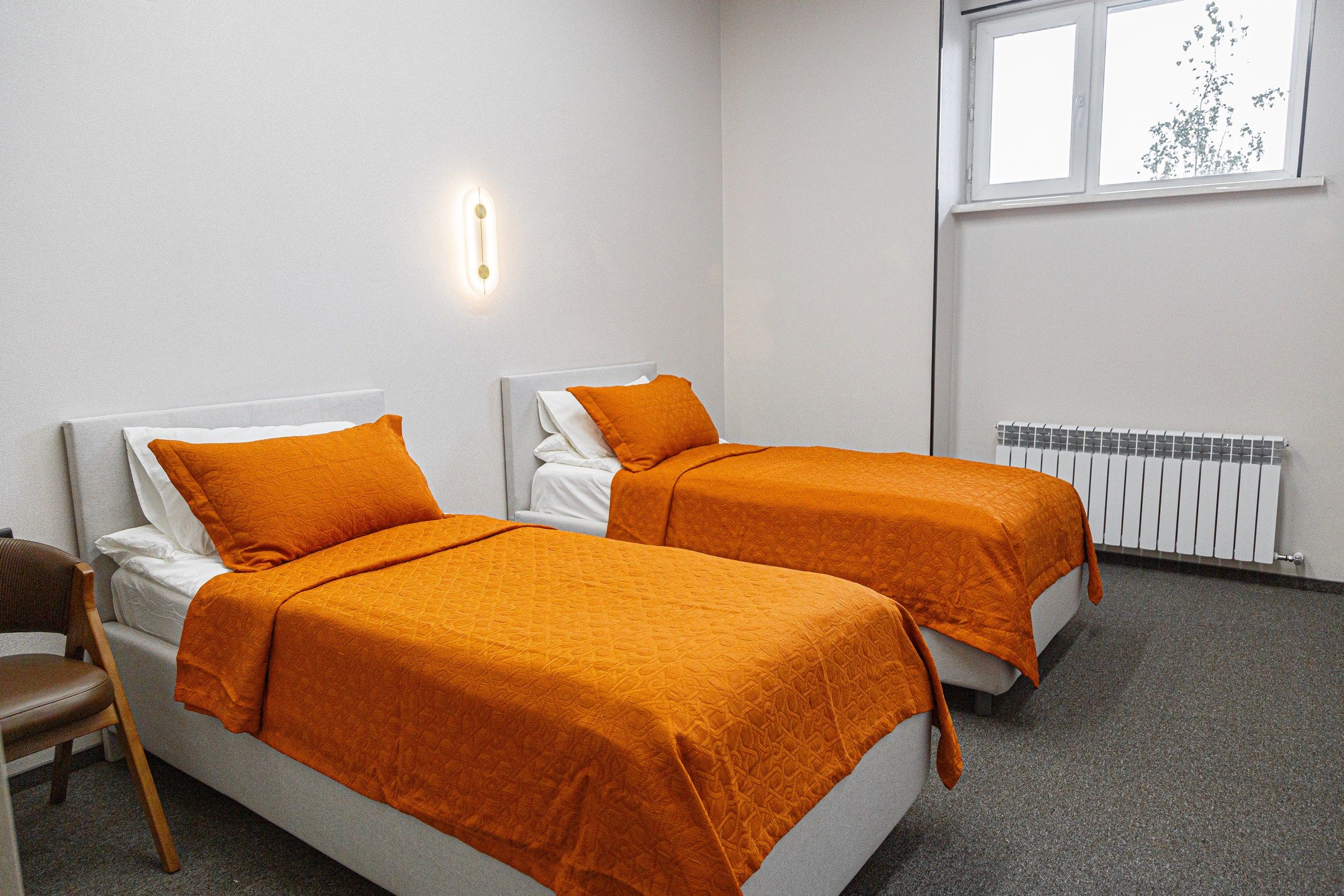 Habitación doble con dos camas, ventana y radiador.