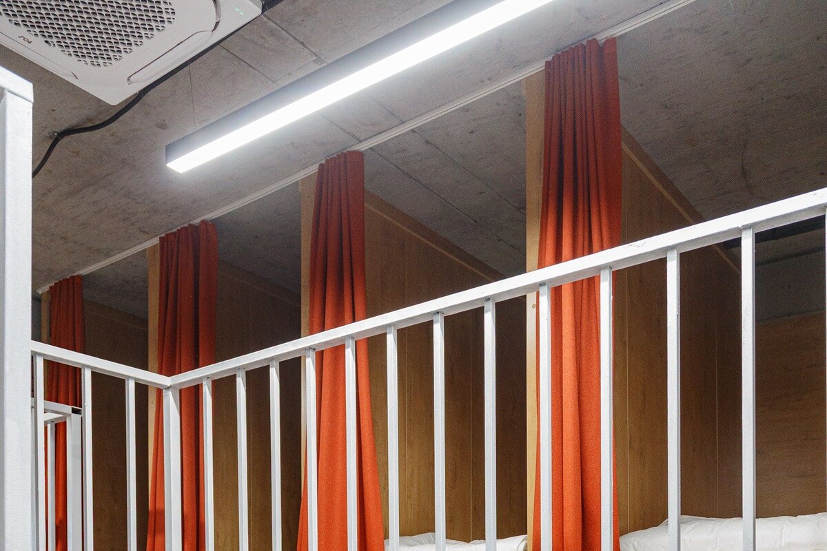 A dormitory room with bunk beds, red curtains, and a ceiling fan.