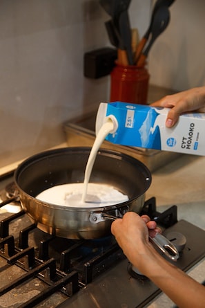Una persona vertiendo leche en una olla sobre la estufa.