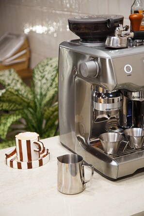A coffee machine with a control panel, a coffee pot, and two metal cups on a countertop. - Tamga Hostel Bishkek (Bishkek)