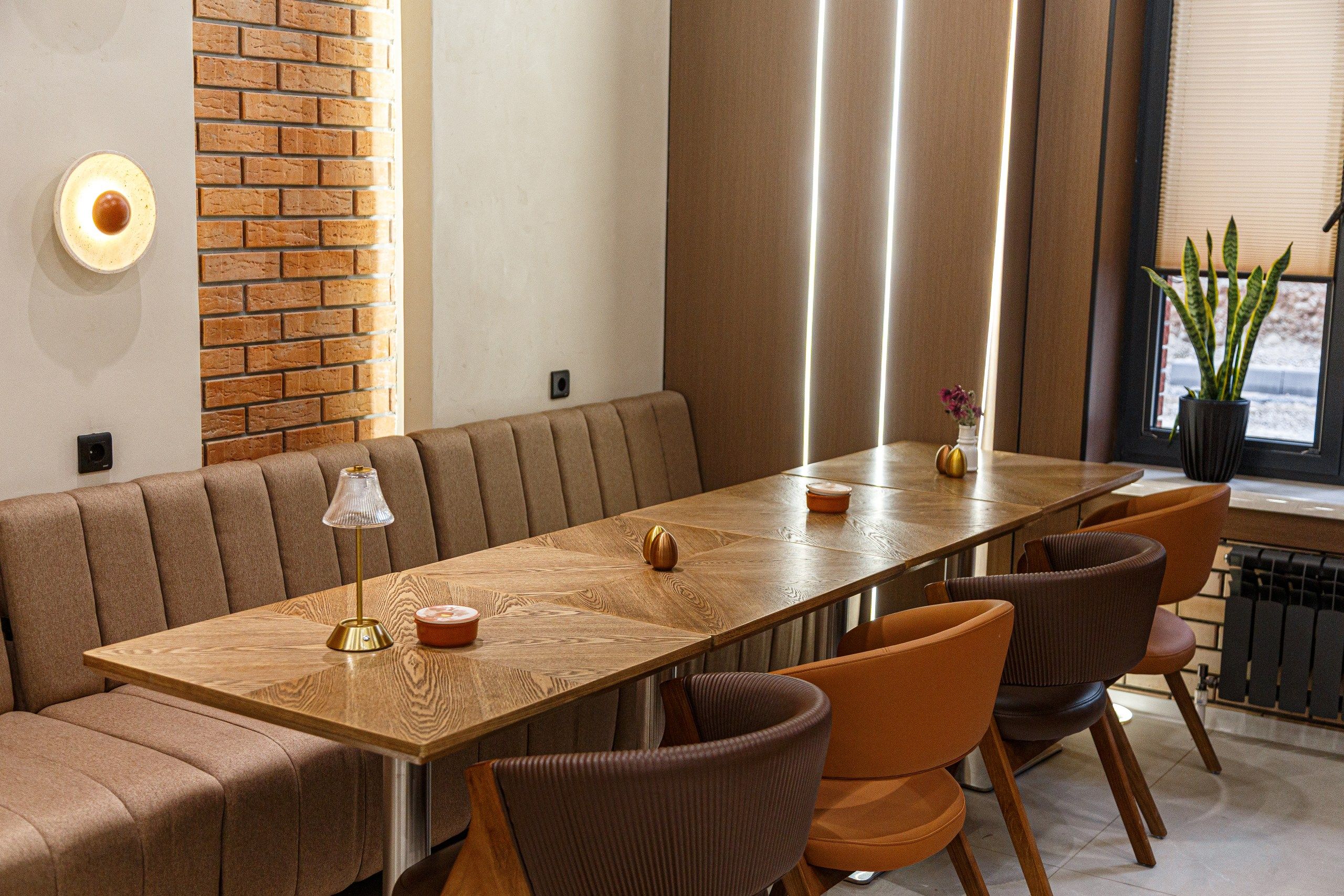 A modern dining area with a long wooden table, cushioned seating, and a brick accent wall.