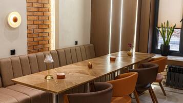 A modern dining area with a long wooden table, cushioned seating, and a brick accent wall.