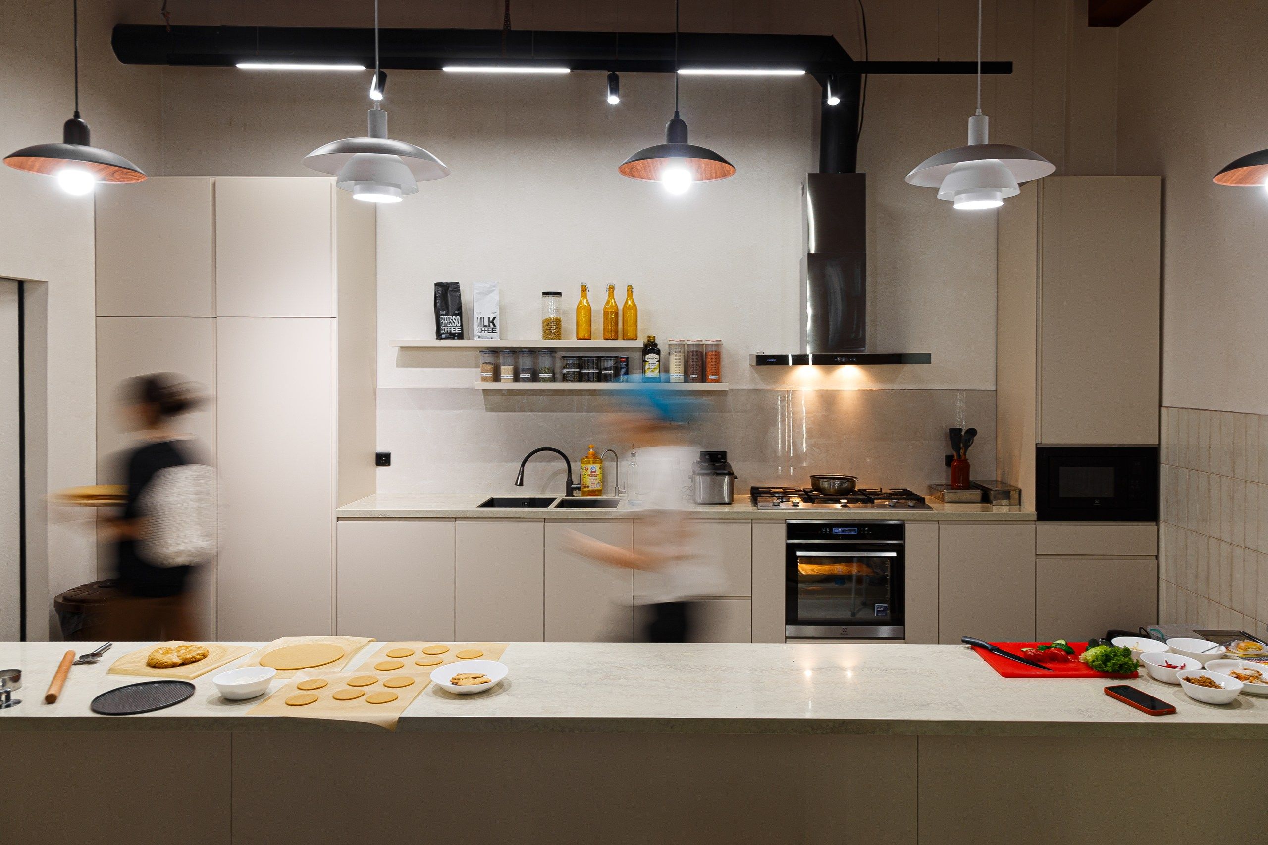 A modern kitchen with pendant lighting, a stainless steel range hood, and a variety of kitchen appliances.
