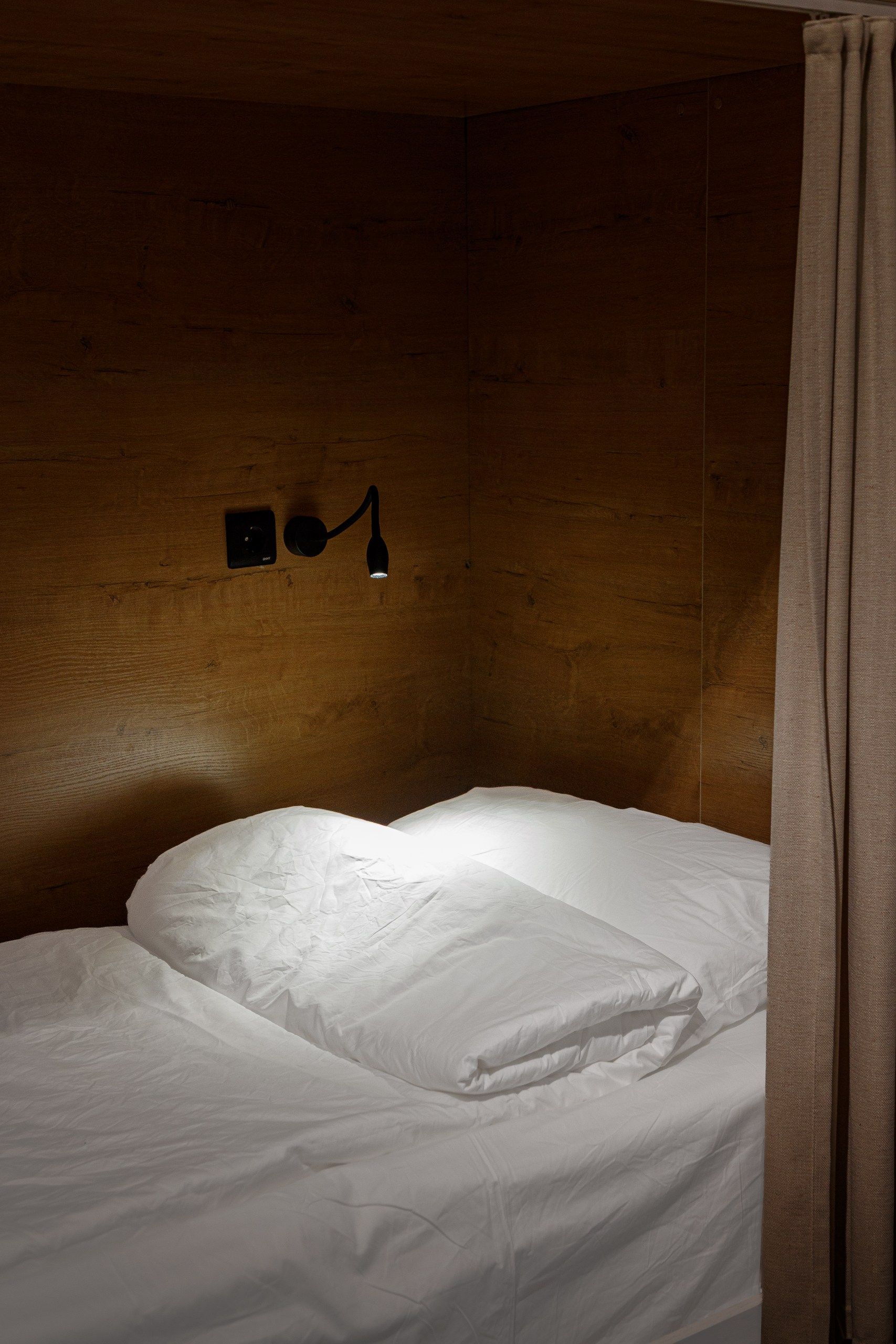 A single bed with white bedding in a room with wooden walls and a wall-mounted light fixture.