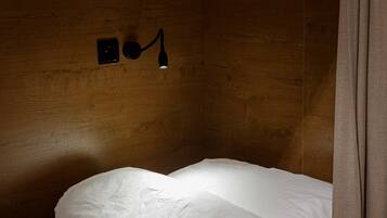 A single bed with white bedding in a room with wooden walls and a wall-mounted light fixture.