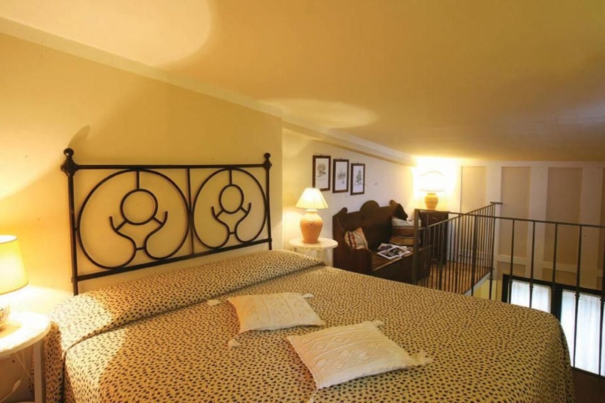 Habitació d'hotel amb llit, una petita taula de nit, una làmpada, una cadira, escriptori i un balcó.
