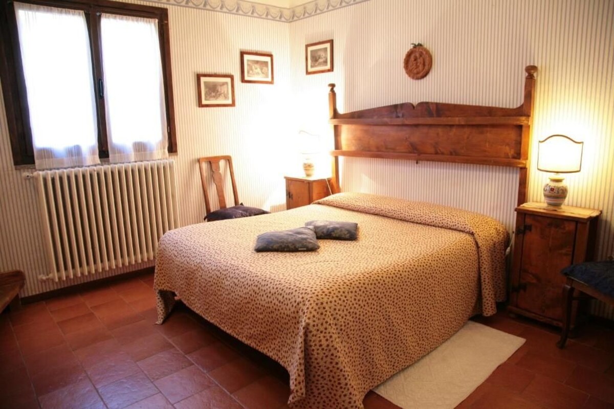Un dormitori amb un llit, un radiador, una finestra i un panell de capçal de fusta.