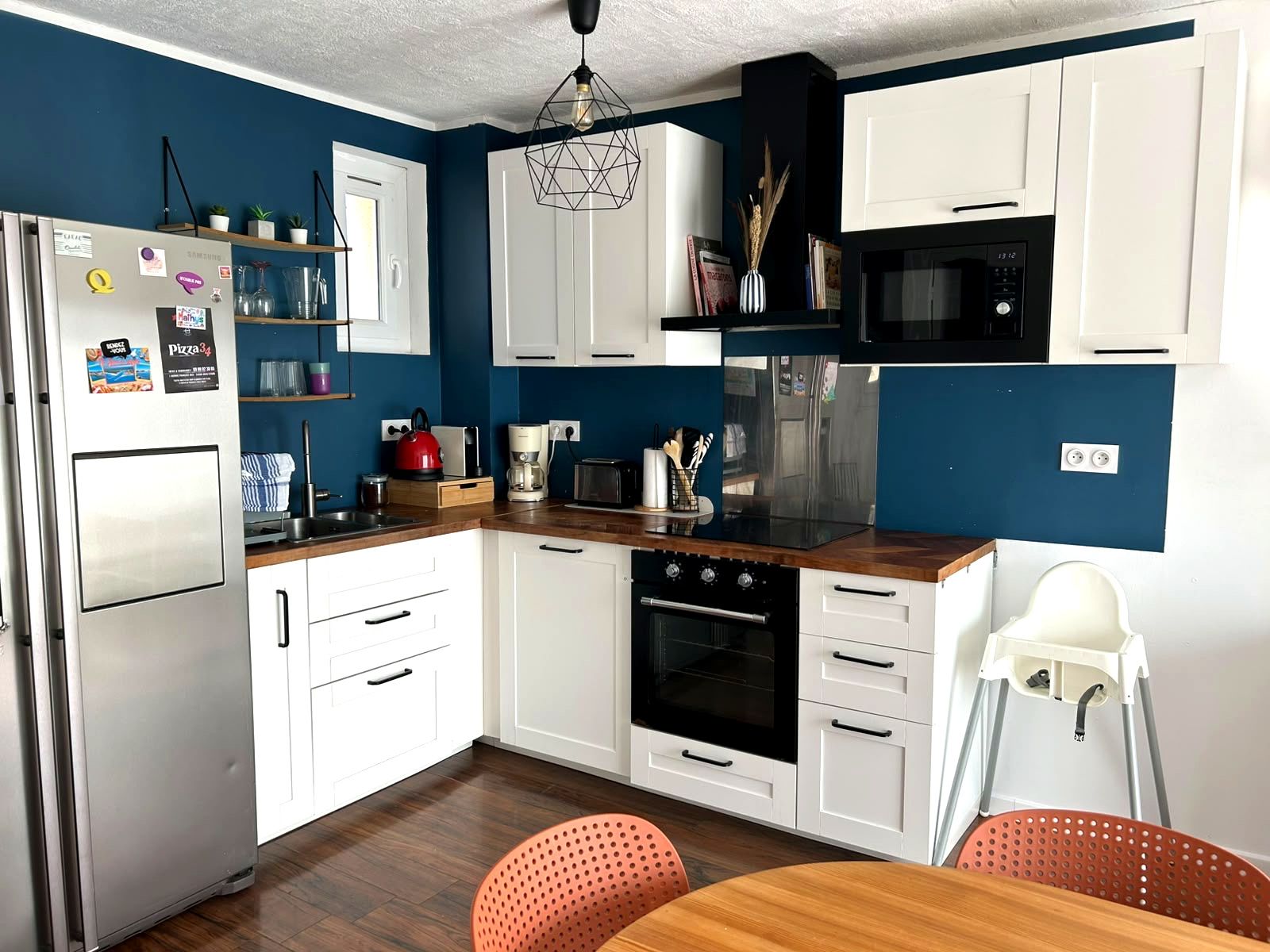 A modern kitchen with white cabinets, a stainless steel refrigerator, a microwave, an oven, and a coffee maker.