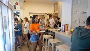 Un espace cuisine moderne où l’on voit des personnes en train de manger, un réfrigérateur et un comptoir avec des aliments.