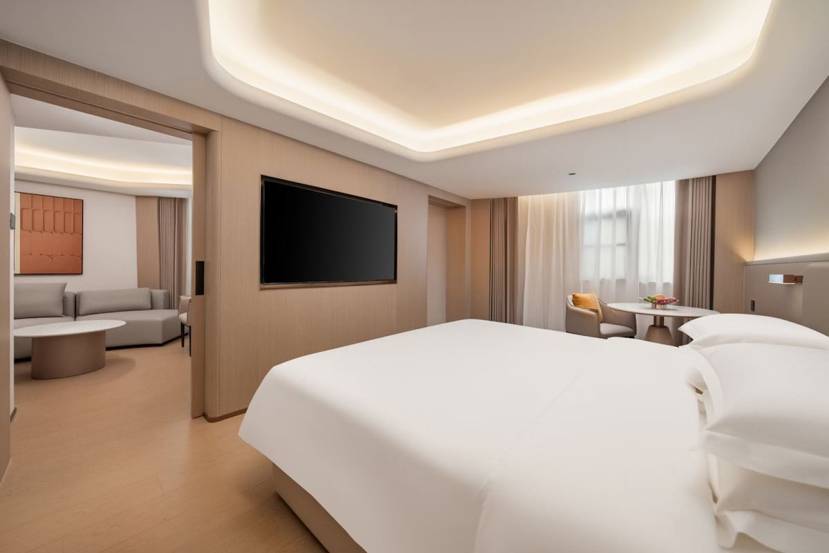 Una camera d'hotel con un letto grande, una televisione, un'area salotto con divano e poltrone e un tavolo da pranzo con una ciotola di frutta.