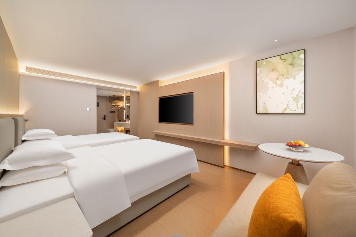 Una camera d'albergo con un letto, una TV a parete, un tavolino con della frutta e un quadro.