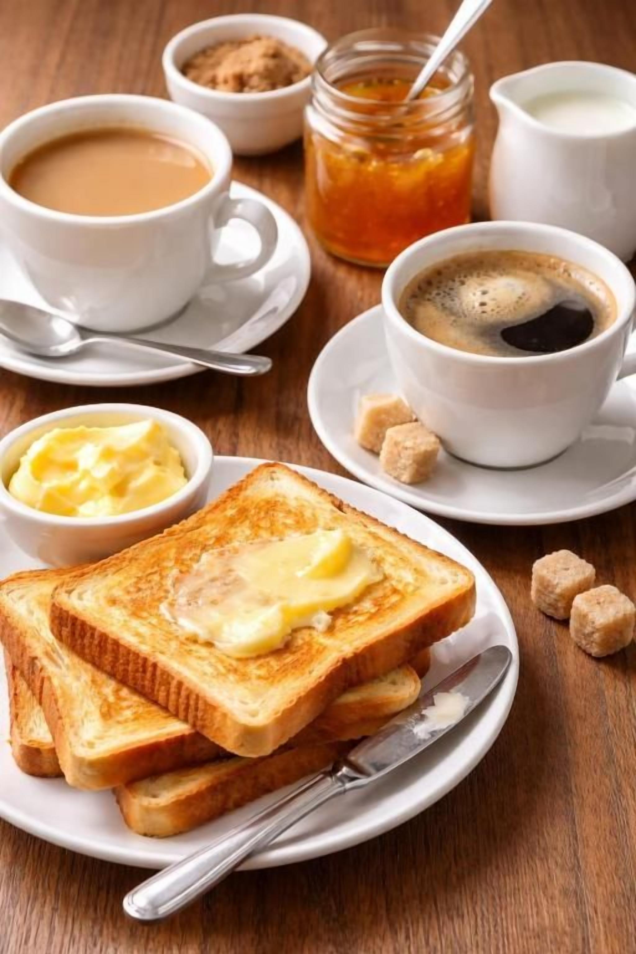 Desayuno con tostadas, mantequilla, café y terrones de azúcar sobre una mesa de madera.