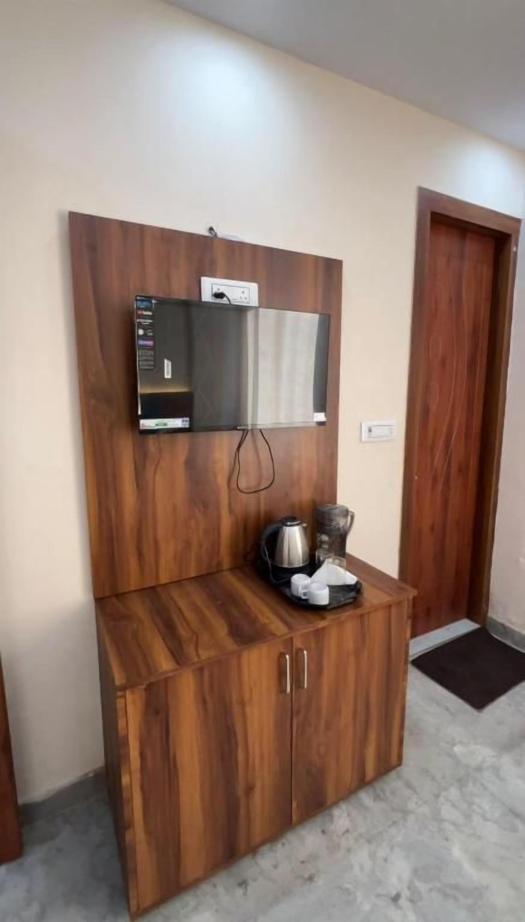 Un mueble de madera con un televisor de pantalla plana montado encima, una tetera y una taza sobre el mueble.