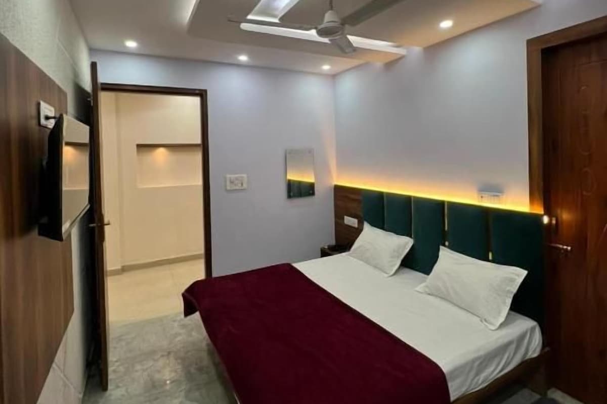 A modern bedroom with a bed, a ceiling fan, recessed lighting, and a door leading to another room.