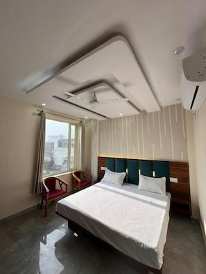 A hotel room with a large bed, a ceiling fan, a window with curtains, and a view of the city. - Hotel The Vrnda Heritage (Motichur Range)