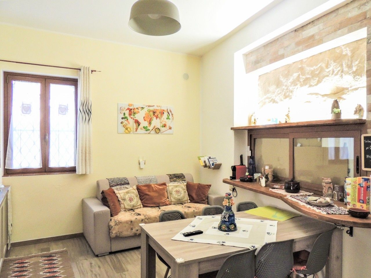 A living room with a sofa, a dining table, and a kitchen area with a counter and shelves.