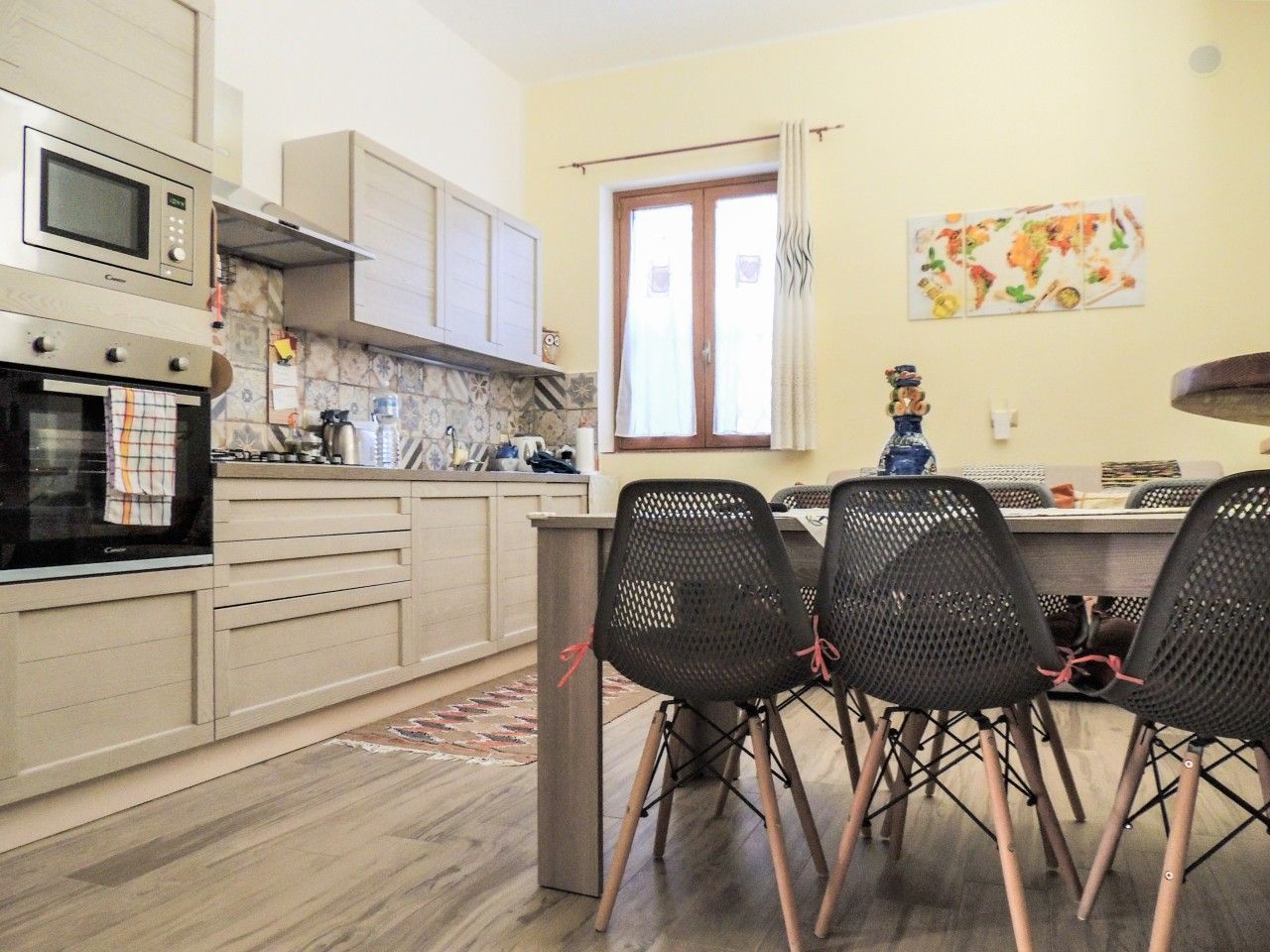 A kitchen with a microwave, oven, and stove, a dining area with chairs, and a window with curtains.