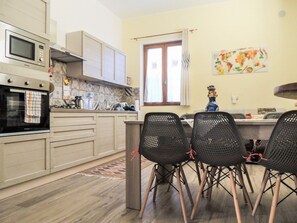 A kitchen with a microwave, oven, and stove, a dining area with chairs, and a window with curtains. - Porta Nord Lodge - A Historic Residence Nestled in the Castle Rock in Sperlinga (Sperlinga)