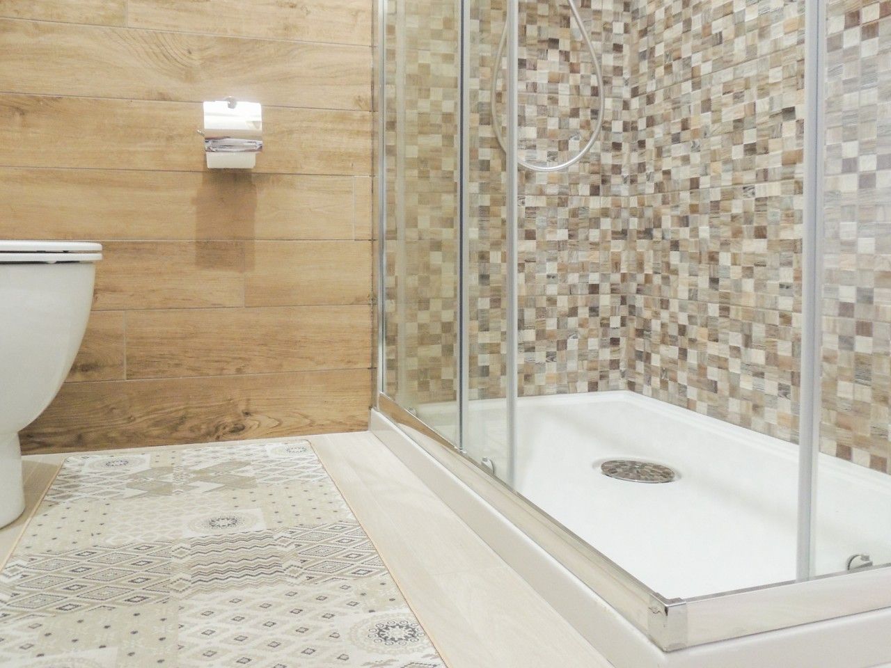 A bathroom with a shower enclosure, a toilet, and a patterned floor.