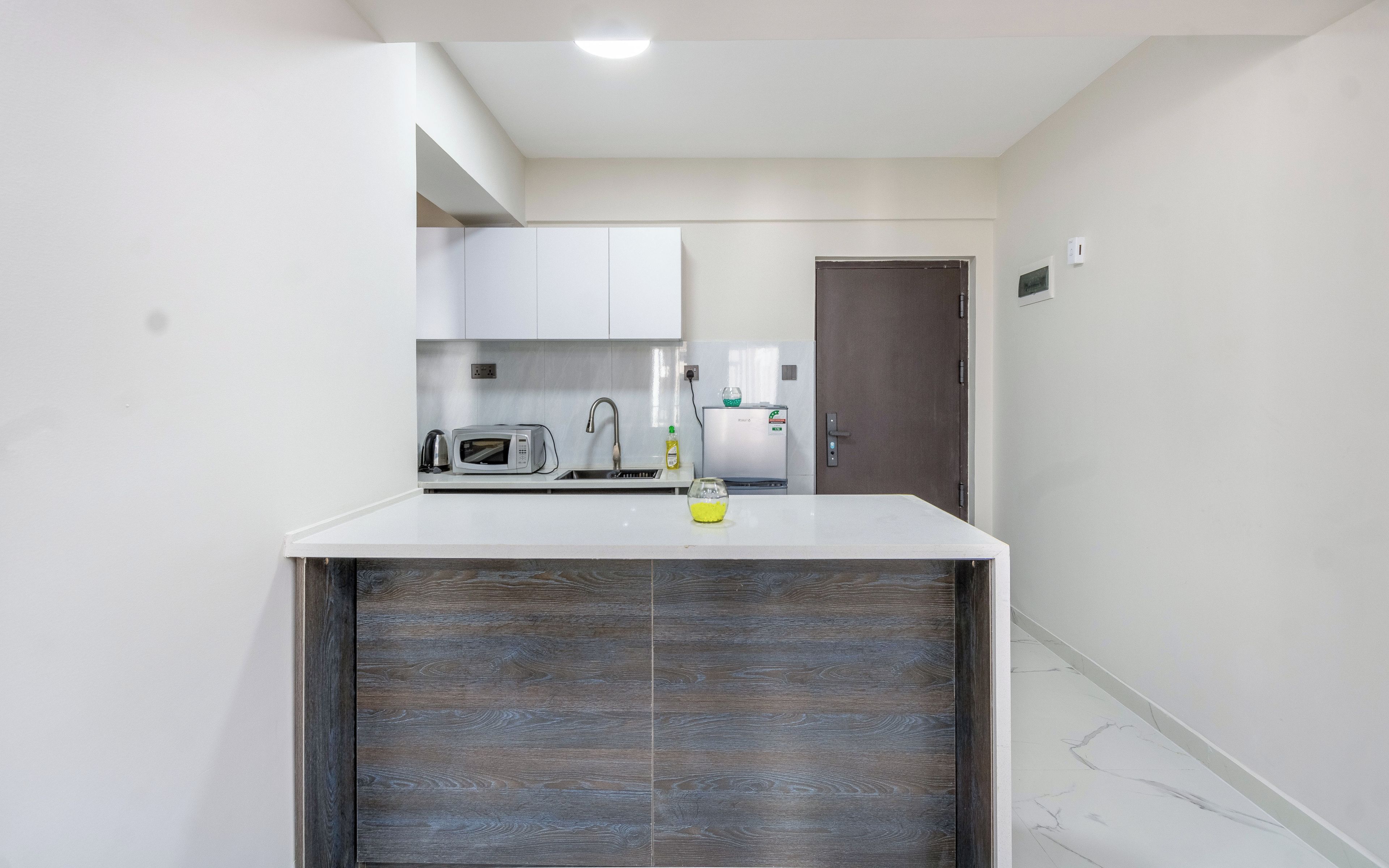 A compact kitchen with white cabinets, a microwave, a kettle, and a refrigerator.