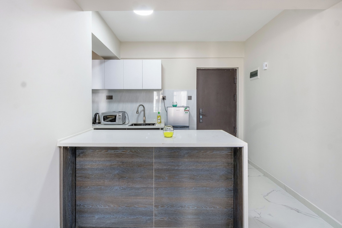 A compact kitchen with white cabinets, a microwave, a kettle, and a refrigerator.
