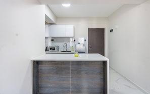 A compact kitchen with white cabinets, a microwave, a kettle, and a refrigerator. - Kindaruma homes apartments  (Nairobi)