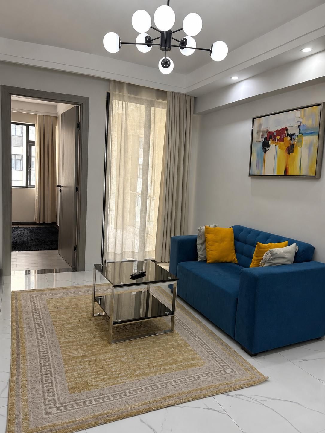 A modern living room with a blue sofa, a glass coffee table, and a contemporary chandelier.