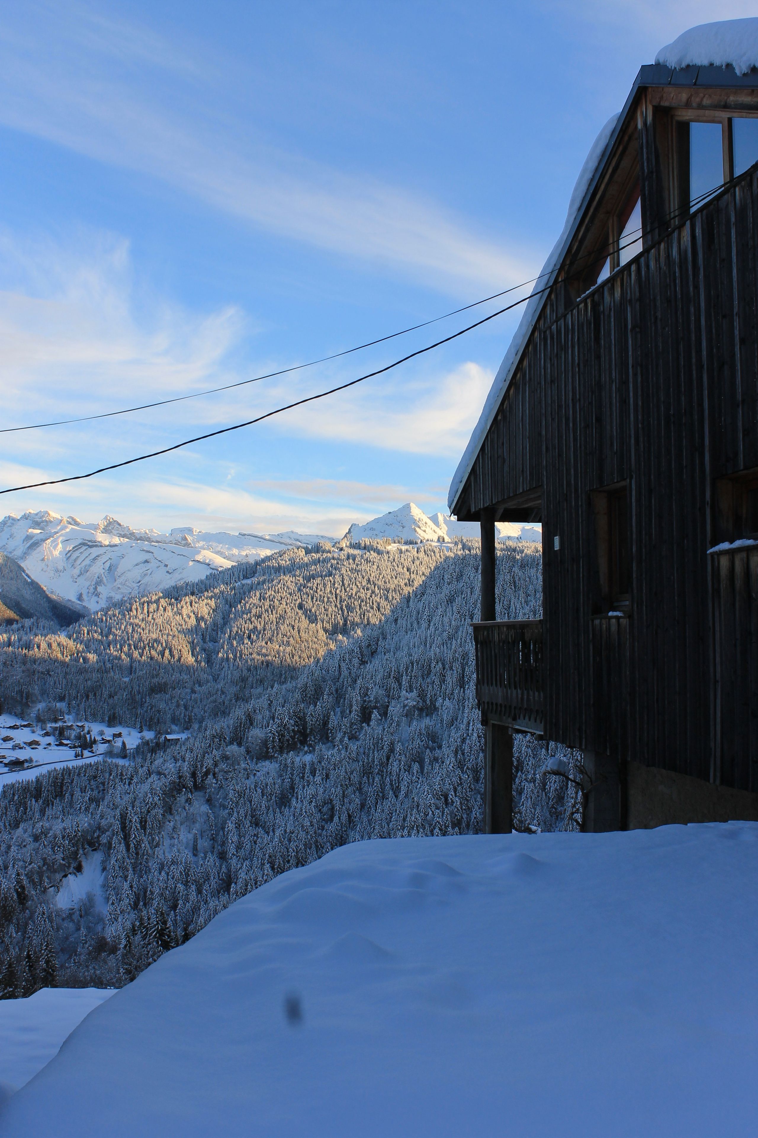 Een houten chalet met een balkon met uitzicht op een besneeerd berglandschap.