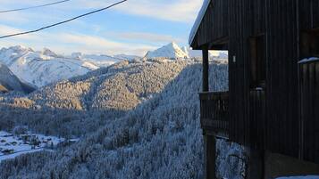 Een houten chalet met een balkon met uitzicht op een besneeerd berglandschap.
