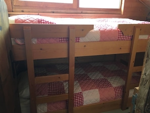 Un lit superposé avec un matelas matelassé et une étagère inférieure sur laquelle est posée une couverture à motifs.