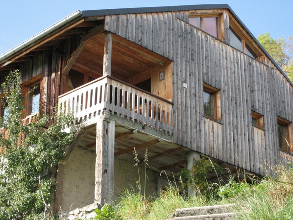 Une cabane en bois rustique dotée d’un balcon, de fondations en pierre et surplombant un ciel dégagé.