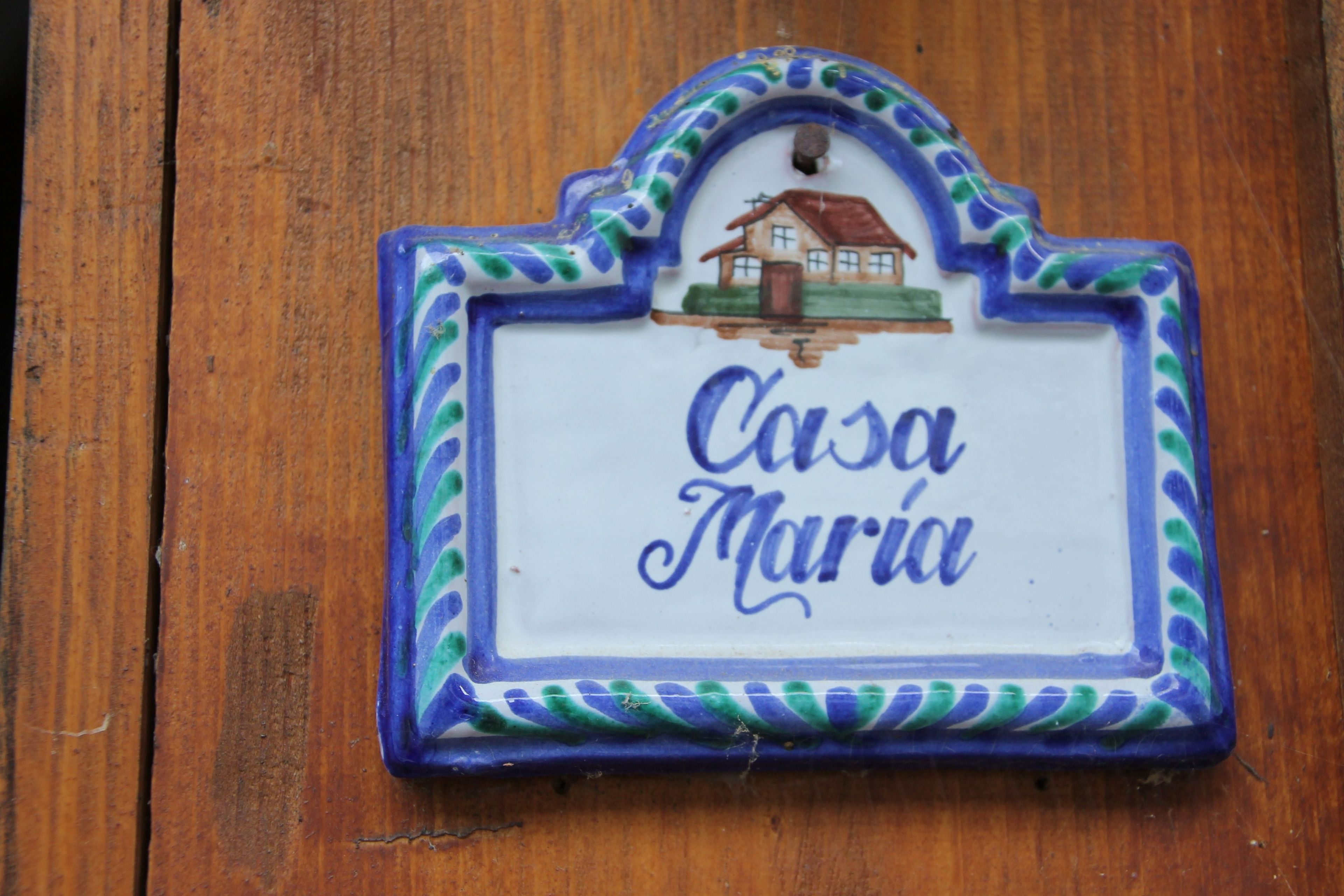 A ceramic sign with 'Casa María' written on it, featuring a house illustration and decorative border.