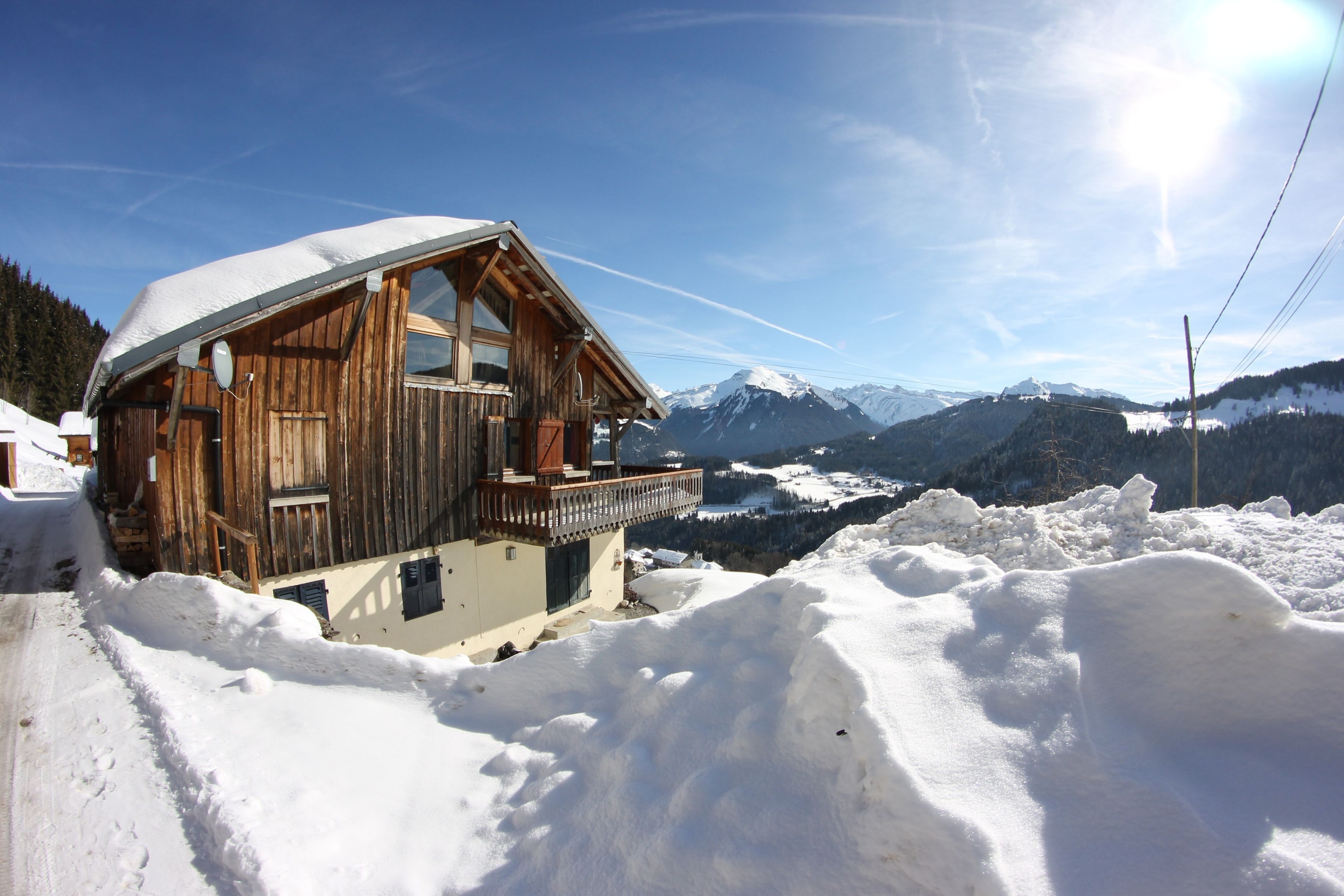Un chalet en bois doté d’un balcon, entouré de montagnes enneigées et surplombant un ciel dégagé.