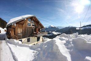 Un chalet en bois doté d’un balcon, entouré de montagnes enneigées et surplombant un ciel dégagé.