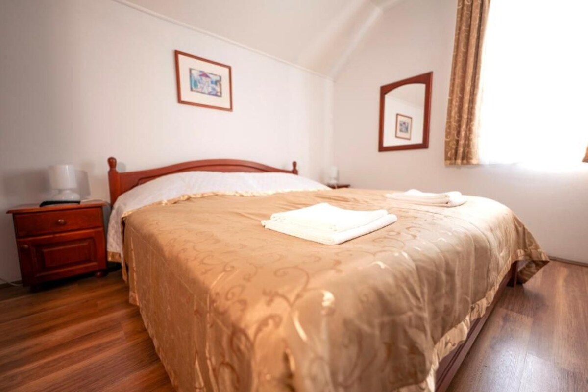 A bedroom with a wooden bed, a nightstand, a bedside table, and a window with curtains.