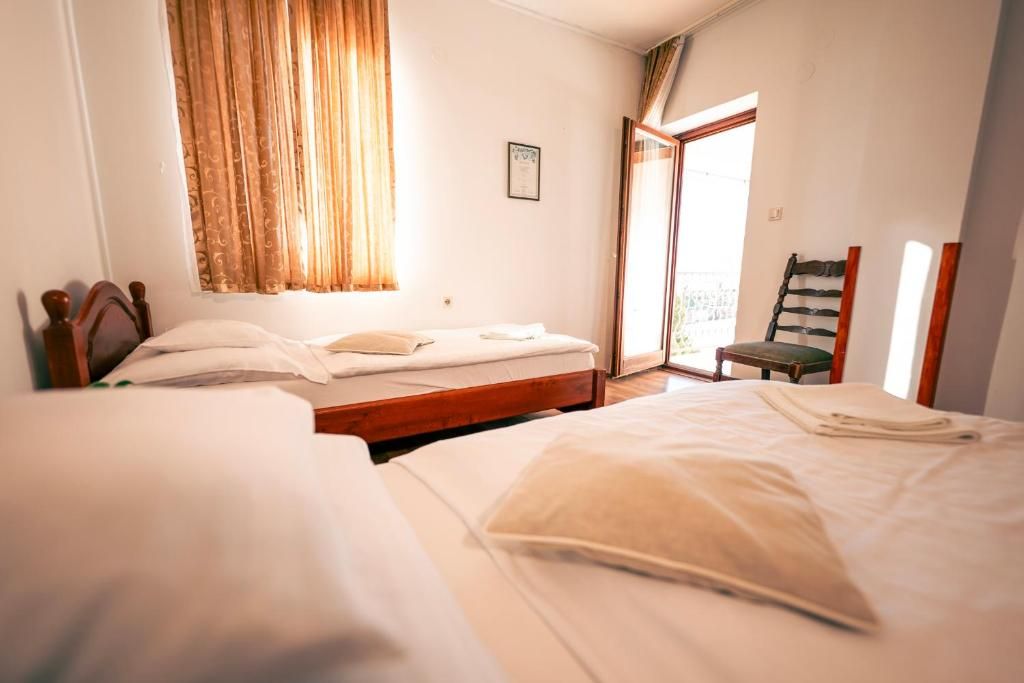 Quarto de hotel com duas camas, janela com cortinas, uma cadeira e porta que dá para o exterior.