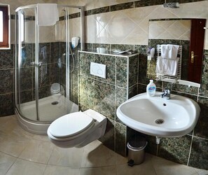 A bathroom with a glass-enclosed shower, a white toilet, a sink with a mirror, and a towel rack. - Polgár Elixír Hotel  (Villány)