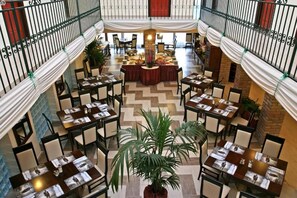 A multi-level dining area with tables set for guests, featuring a central decorative column and potted plants. - Polgár Elixír Hotel  (Villány)