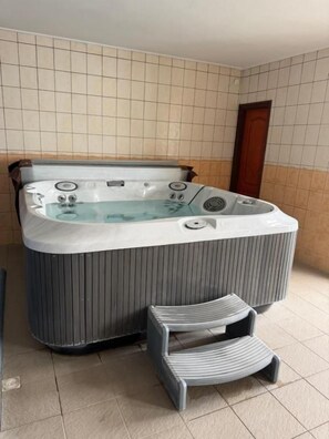 A hot tub with a seating area, a tiled wall, and a wooden door. - Polgár Elixír Hotel  (Villány)