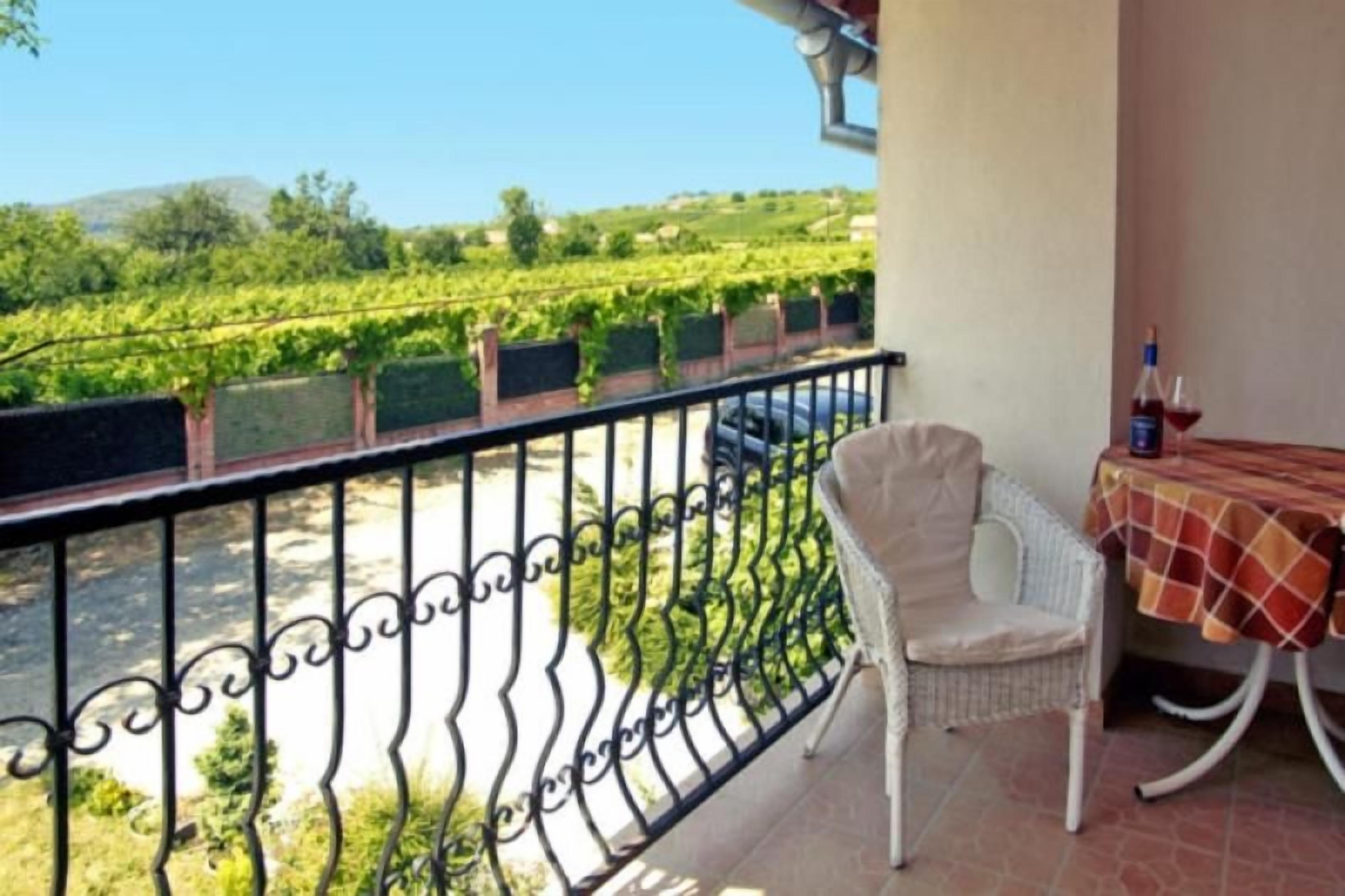 A balcony with a wrought iron railing, a wicker chair, and a table with a checkered tablecloth.
