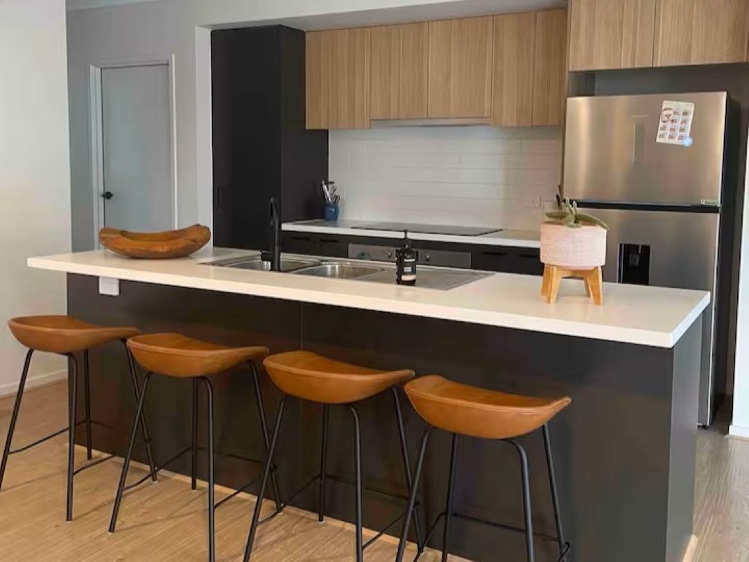 Une cuisine moderne dotée d’un îlot central, de tabourets de bar, d’un réfrigérateur en acier inoxydable et d’armoires en bois.
